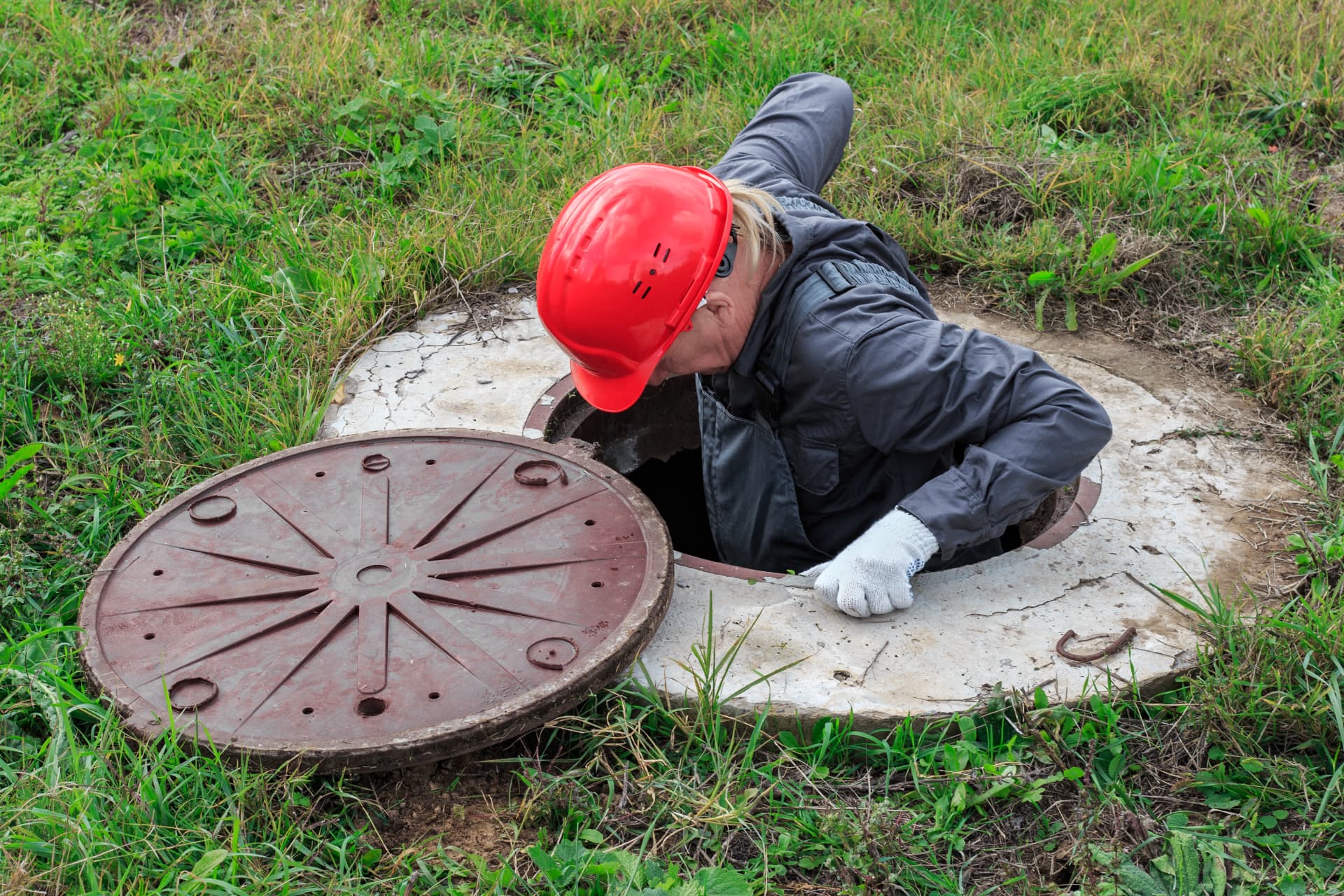 Technician in a red hard hat entering a tank access chamber