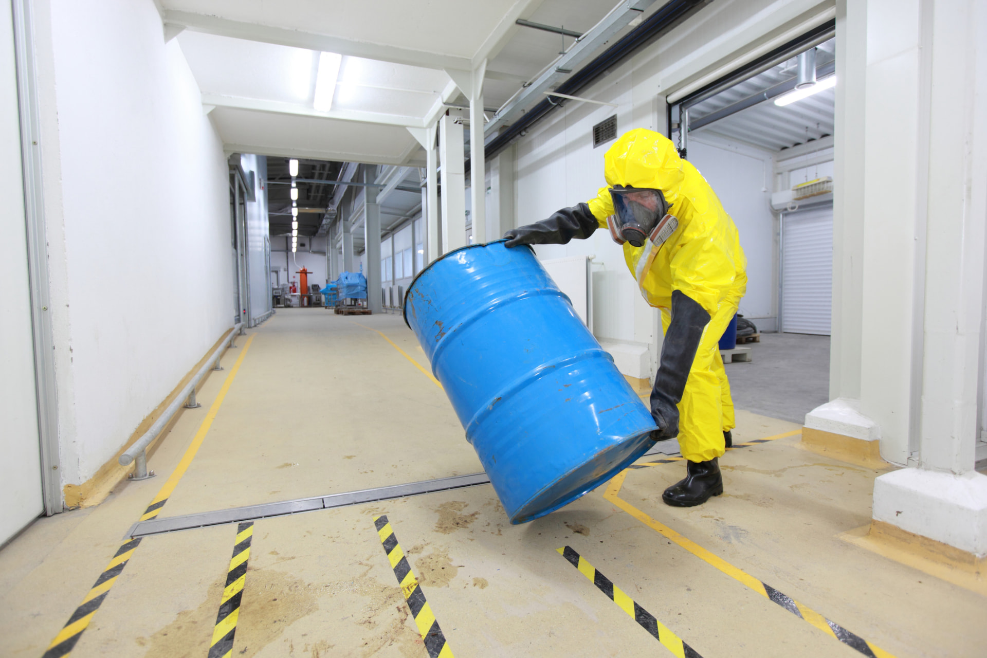 Technician in protective gear moving a fuel drum in a containment bay