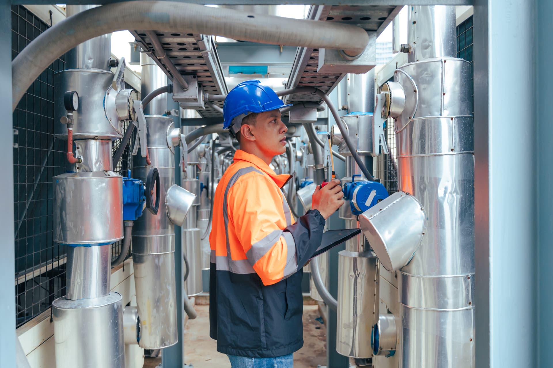 Technician inspecting insulated piping and valves in a plant room
