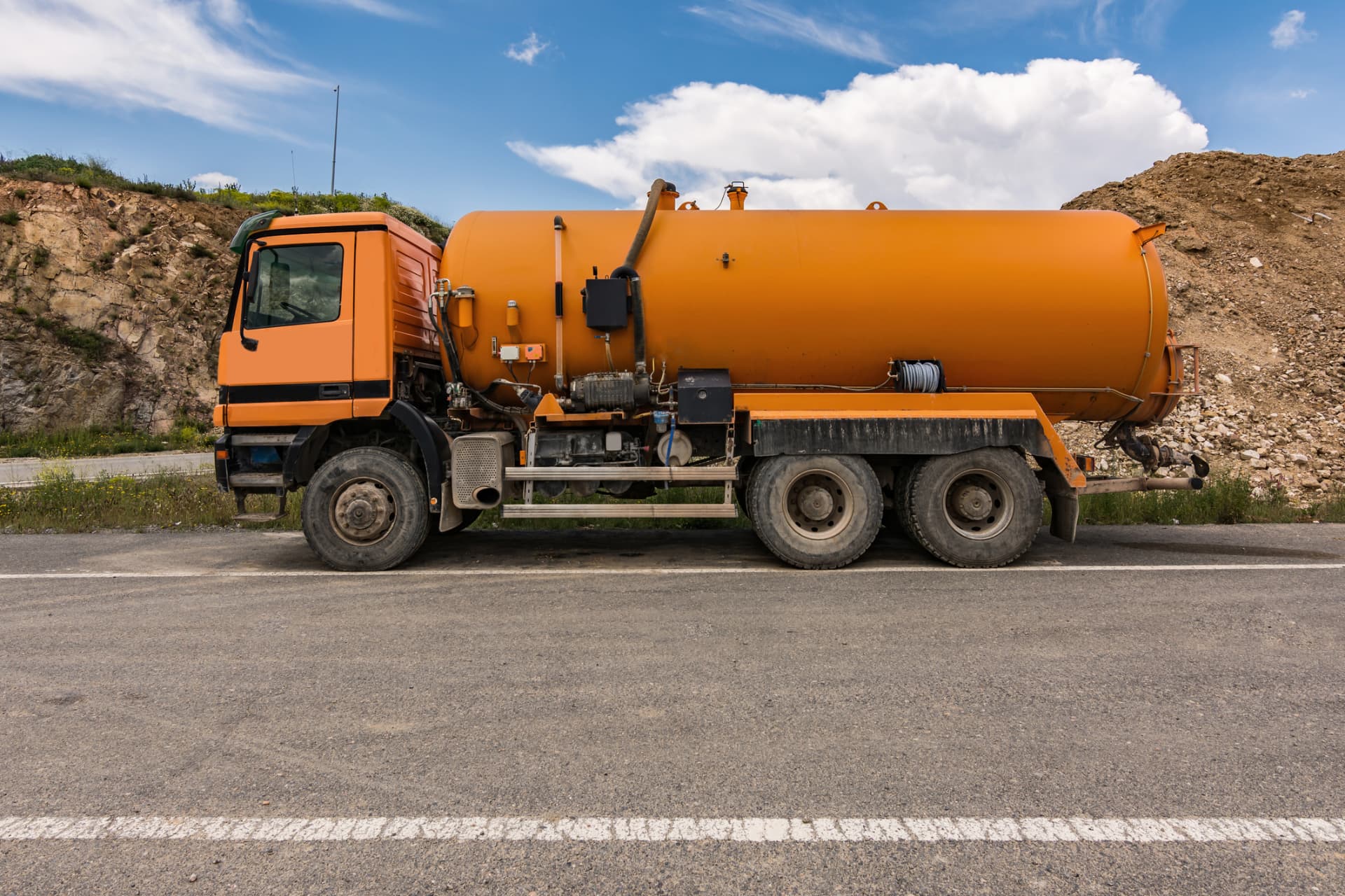 Orange vacuum tanker truck parked on a roadside