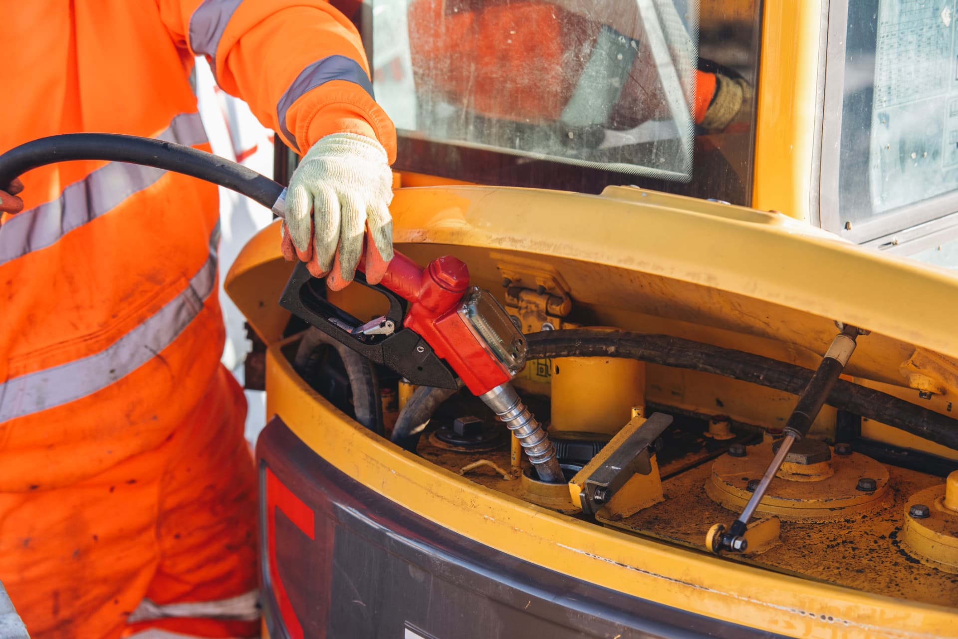 Worker refueling yellow heavy equipment from a diesel nozzle